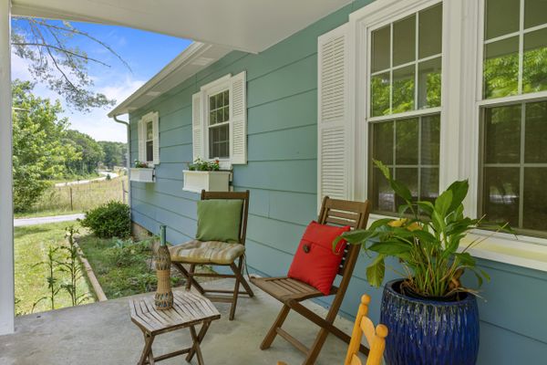 Cozy porch with wooden chairs and colorful cushions overlooking a green yard.