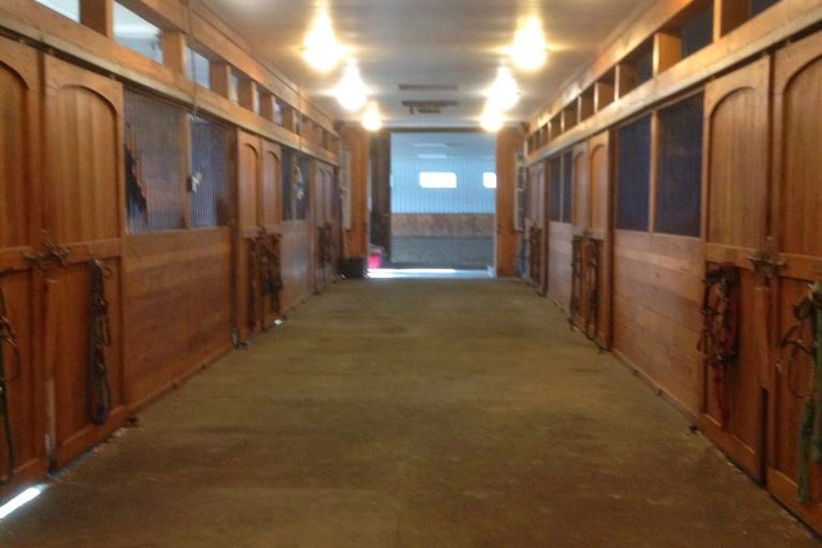 a well-lit barn aisle ending with double doors opening into an indoor arena