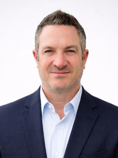 Man in a navy blue suit and light blue shirt against a plain white background.