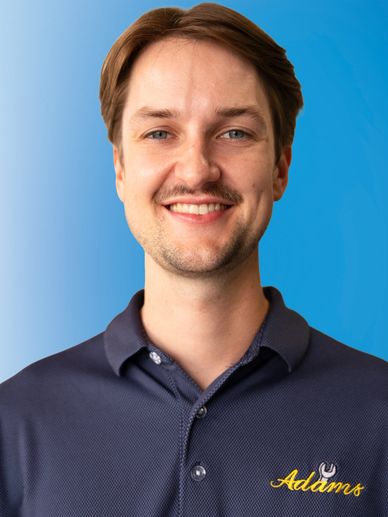 Smiling man in a navy blue Adams polo shirt against a blue gradient background.
