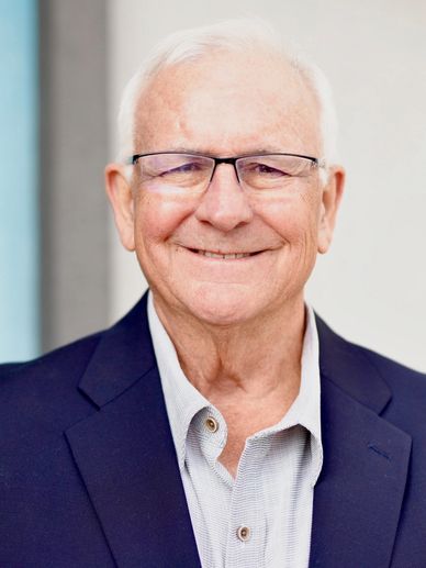 Smiling elderly man wearing glasses and a navy blazer.