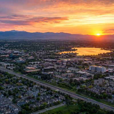 A vibrant sunset over a suburban city with mountains and a lake in the background.