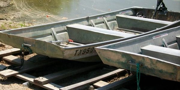 Two aluminum boats resting on wooden rails near water.