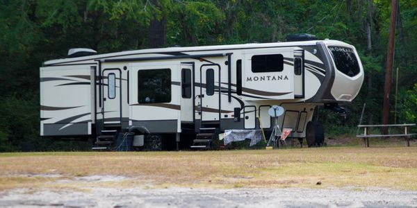 A Montana RV parked in a wooded area with outdoor furniture nearby.