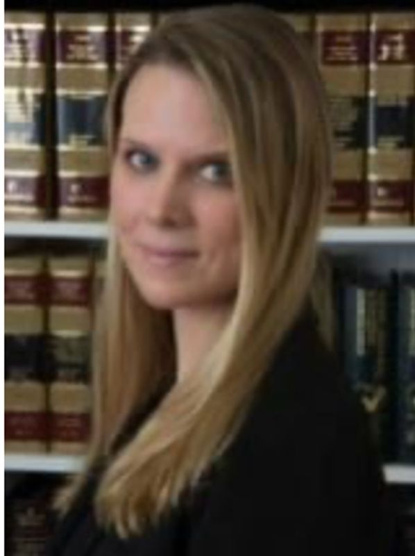 Professional woman with blonde hair stands in front of law books.