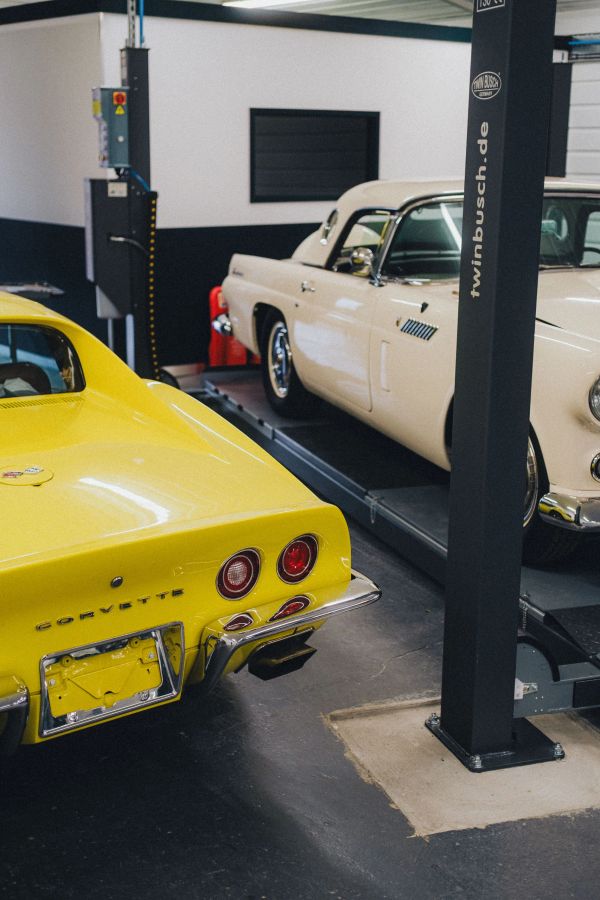Yellow Corvette and cream classic car in a garage.
