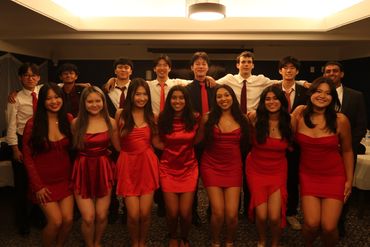 Group of young adults dressed formally, women in red dresses and men in shirts with ties, posing indoors.