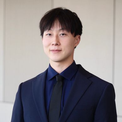 Young man in a navy suit and black tie smiling slightly.