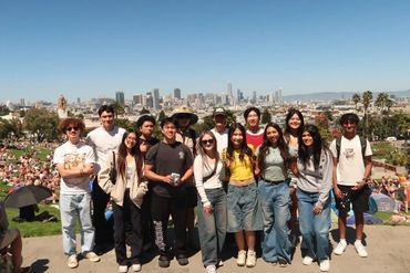 Group of friends posing in a sunny park with a city skyline in the background.