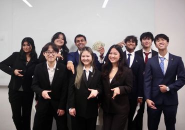 A group of professionally dressed young adults posing and smiling in front of a whiteboard.