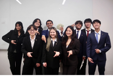 A group of professionally dressed young adults posing and smiling in front of a whiteboard.