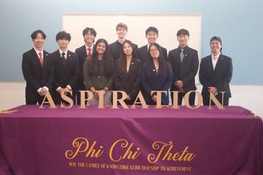 Group of young professionals posing behind a table with the word 'ASPIRATION' and Phi Chi Theta banner.