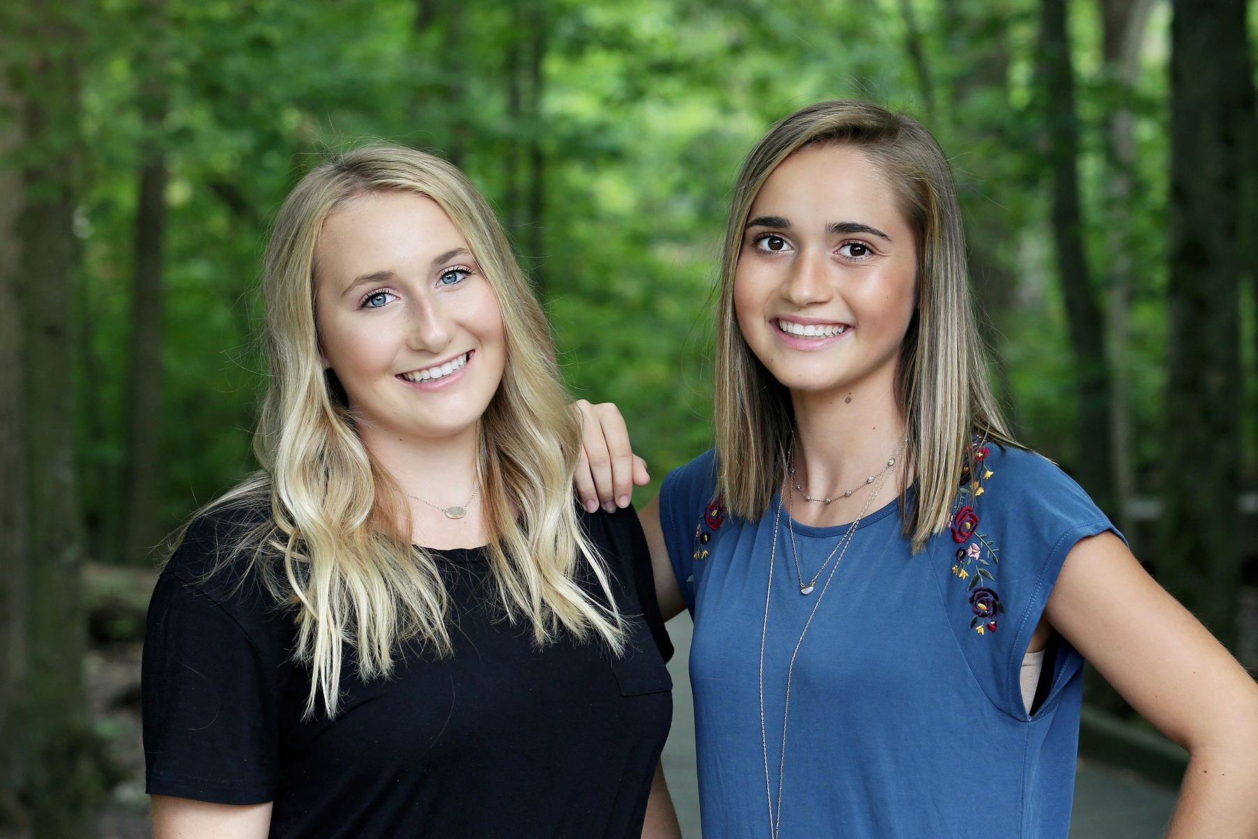 Two young women smiling outdoors with trees in the background.