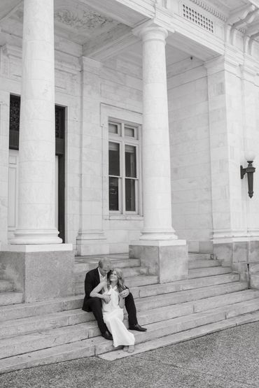 Couple sitting on grand stone steps of a classical building with large columns.
