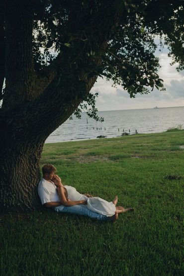 Couple sitting under a tree by the lakeside, sharing a quiet moment.