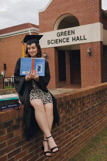 Graduate in cap and gown reading a book outside Green Science Hall.