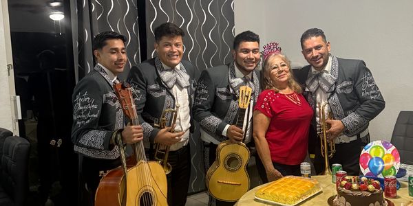 A mariachi band posing with a woman at a birthday party with food and drinks on the table.