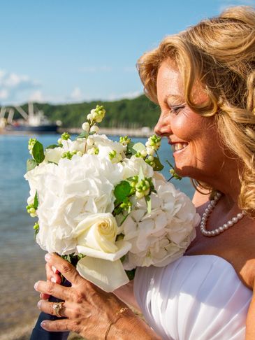 Bride smelling a bouquet of flowers by the water