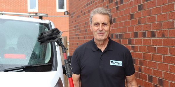 Man in Harley's shirt holding cleaning brush near white van and brick wall.