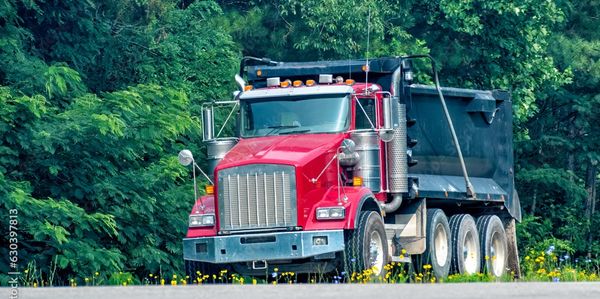 Excavator assisting dirt soil delivery near new construction foundation
