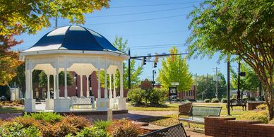 A white gazebo in a sunny park with benches and trees.