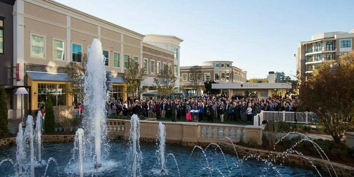 Crowd gathered near a fountain in an urban plaza with shops and apartments.