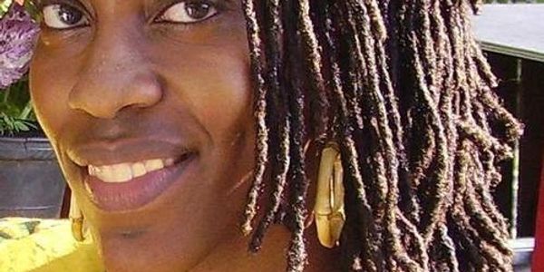 Close-up of a smiling woman with dreadlocks and bamboo earrings.