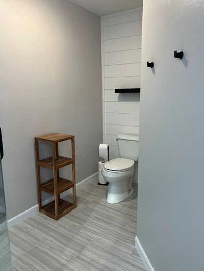 Minimalist bathroom with white toilet, wooden shelving, and gray tiled floor.