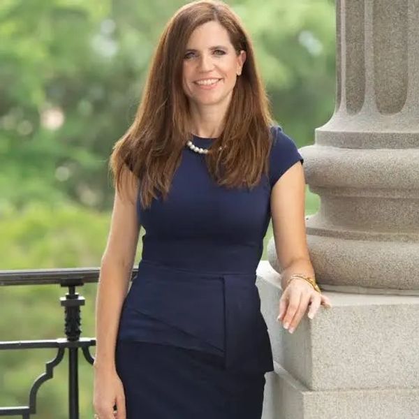 Woman in a navy dress standing by a stone column outdoors.