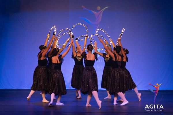 Grupo de dançarinas em vestido preto com arcos de luzes.