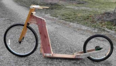 Homemade wooden scooter with two different-sized wheels on a gravel path.