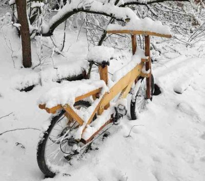 Wooden bicycle covered in snow on a snowy path.