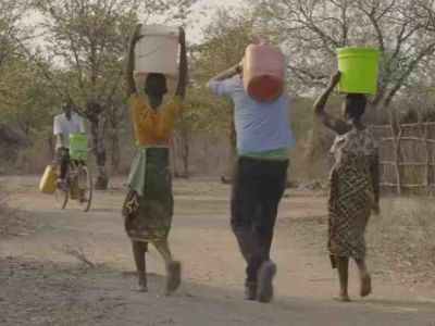 Three people carry water containers on their heads while a person on a bicycle carries a container.