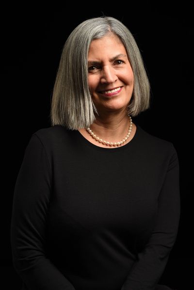 Smiling woman with gray hair wearing a pearl necklace.