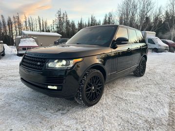 A sleek black Range Rover parked on a snowy ground with headlights on.
