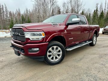 Maroon RAM 2500 pickup truck parked on a gravel road near trees and snow.