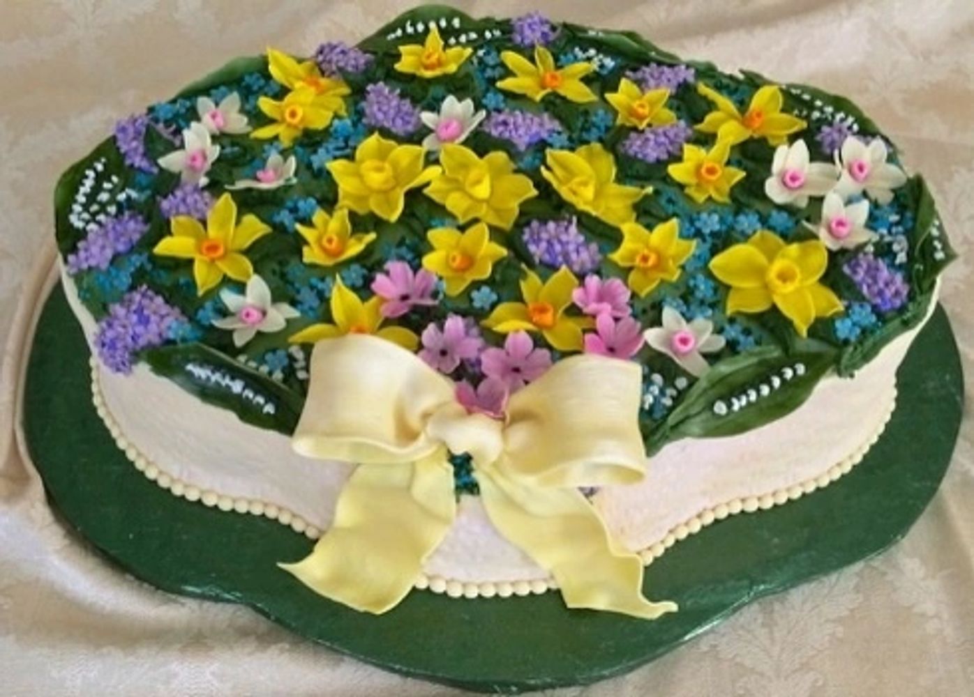 This custom designed cake has Spring buttercream and fondant flowers and adorned with a fondant bow.