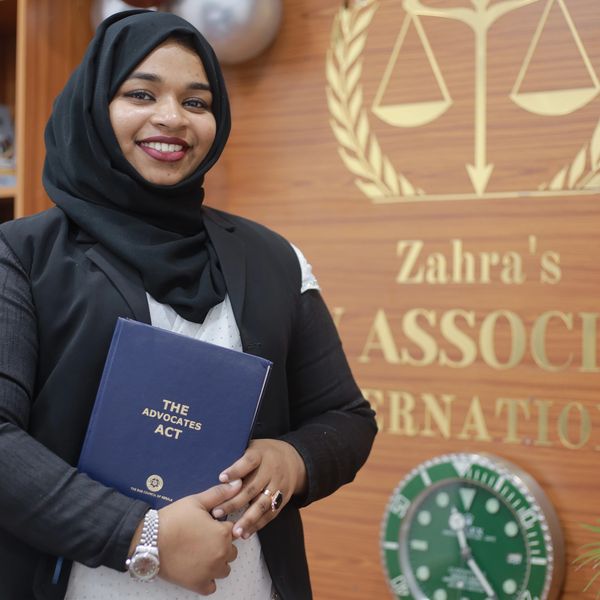 A smiling woman in a hijab holding a book titled 'The Advocates Act'.