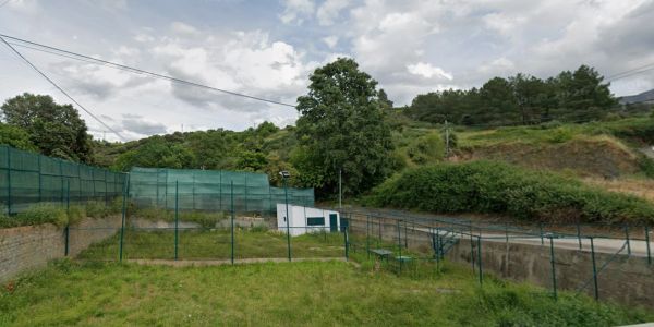 Cancha de tenis sencilla en área rural con vegetación alrededor.