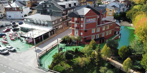 Edificio rojo junto a un río con árboles y una pequeña plaza.