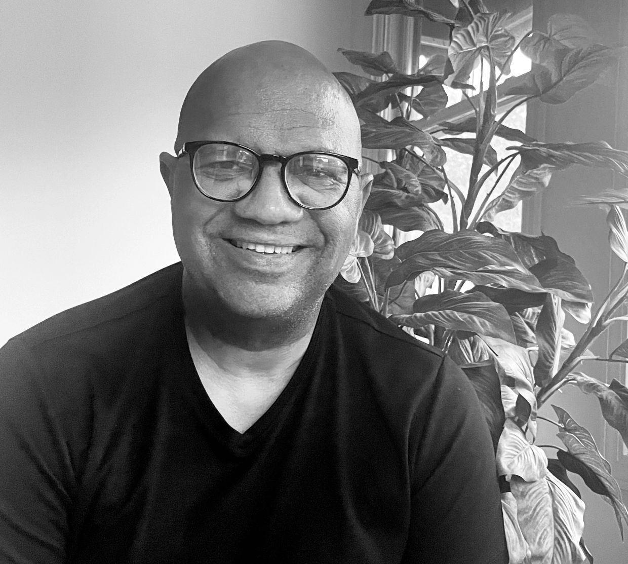 Smiling man wearing glasses in front of a leafy plant.