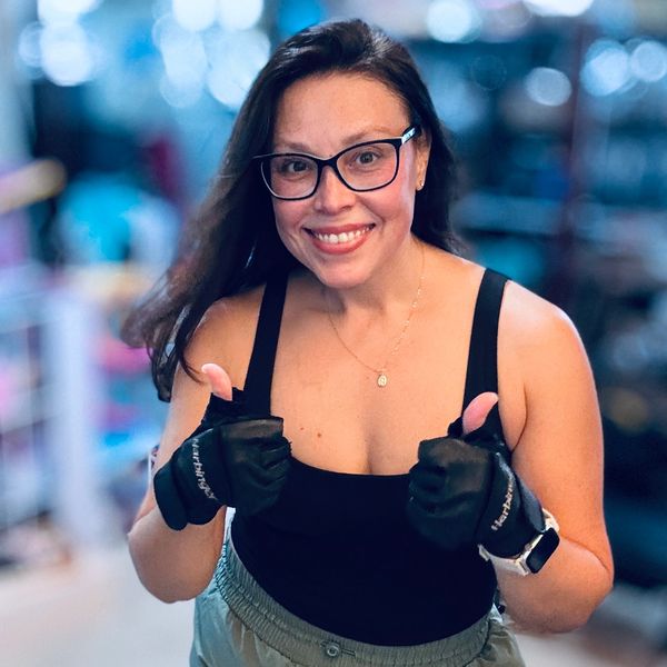 Heather Mewshaw smiling with thumbs up, wearing workout clothes and lifting gloves