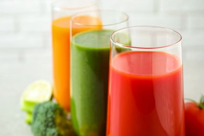 Three glasses filled with red, green, and orange fresh vegetable juices.