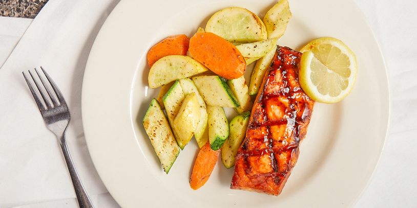 Grilled salmon with roasted vegetables and a lemon slice on a white plate.