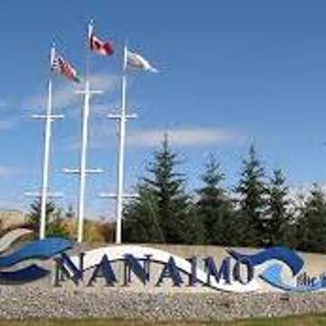 Nanaimo city welcome sign with flags and trees.
