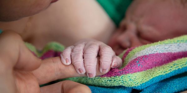 Newborn baby holding parent's finger. Symbol for postnatal care