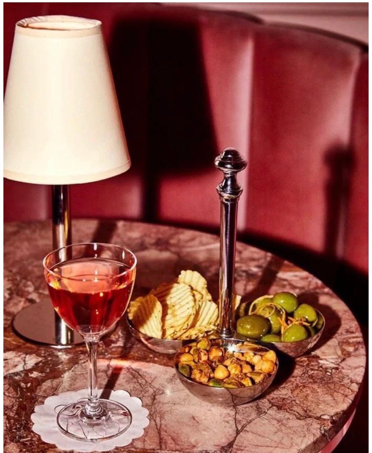 Elegant table setup with a glass of rosé, snacks, and a small lamp.