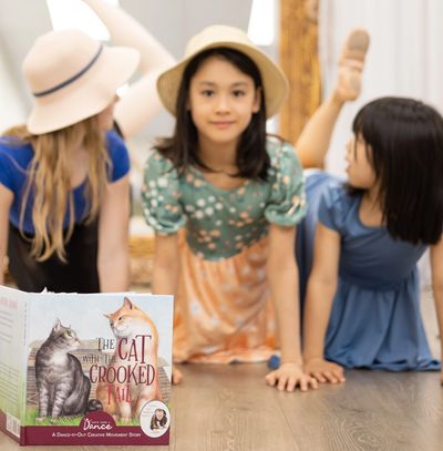 3 girls ages 5-11 reaching their legs behind like a tail and the book cover The Cat with the Crooked