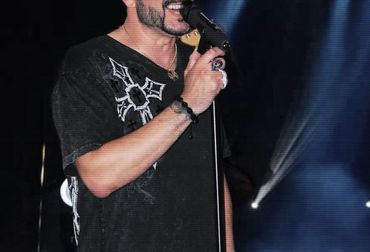 Man singing live on stage with microphone and spotlight.