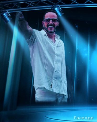 Man in white shirt and sunglasses on stage with blue spotlights.